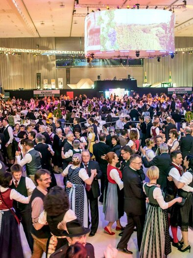 A large crowd is dancing in traditional costumes at an event. The atmosphere is lively and festive, with many dancers in colorful outfits. | © Foto Fischer