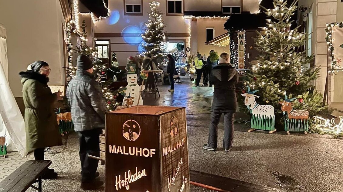 Eine festliche Veranstaltung im Freien mit geschmückten Weihnachtsbäumen und Lichtern. Menschen stehen zusammen und genießen die Atmosphäre. | © MALU