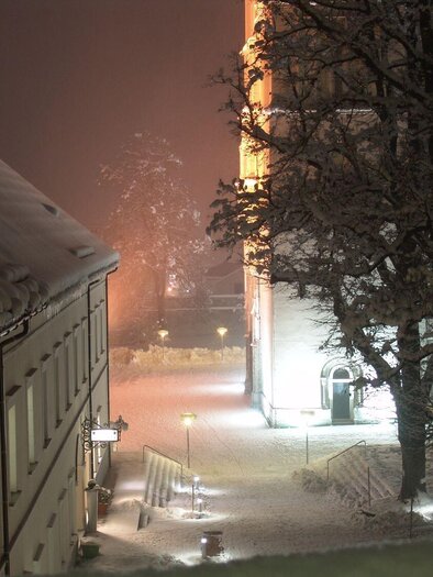 Eine verschneite Straße bei Nacht mit beleuchteten Gebäuden. Die Bäume sind mit Schnee bedeckt und die Szene wirkt ruhig und winterlich. | © Stift Admont
