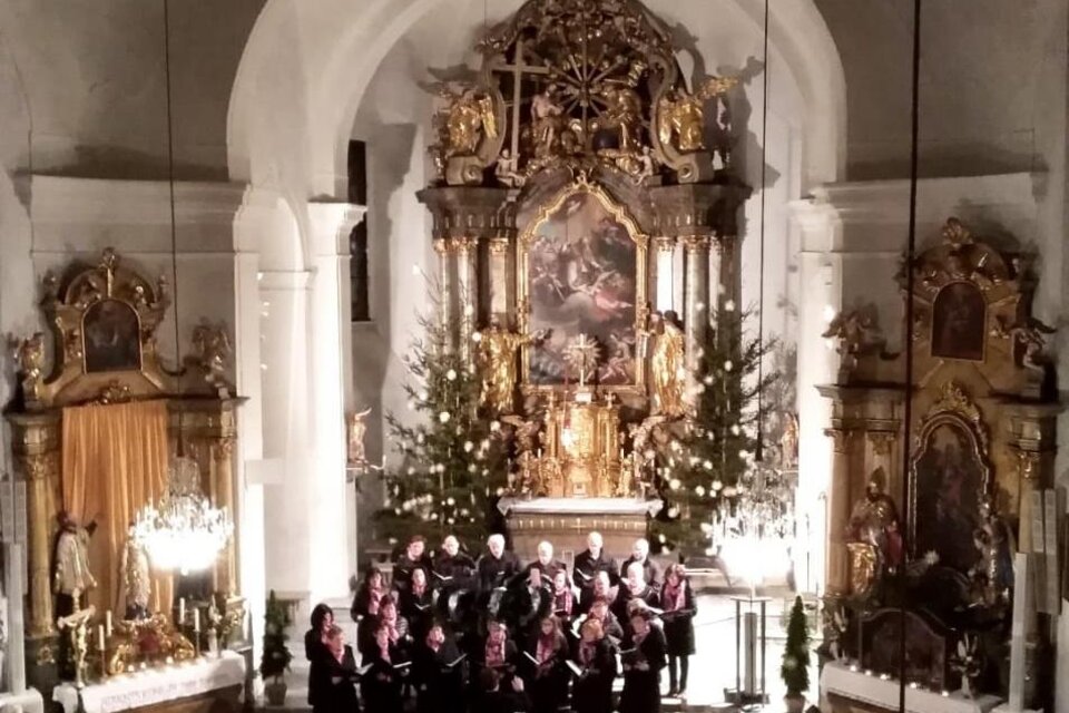 Ein festlicher Chor tritt in einer schönen Kirche auf. Die dekorierte Altaranlage und die mit Lichtern geschmückten Bäume sorgen für eine warme Atmosphäre. | © Singkreis Stubenberg