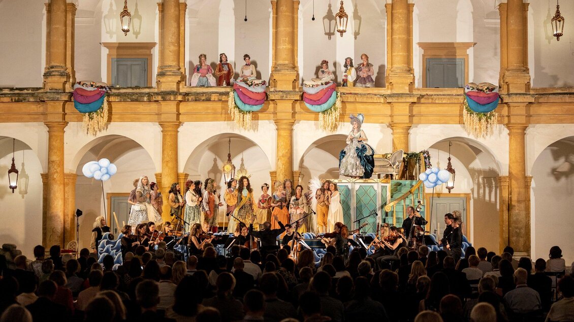 Ein beeindruckendes Bühnenbild mit einer Aufführung und einer großen Menschenmenge. Musiker und Schauspieler interagieren in einer festlichen Atmosphäre. | © Nikola Milatovic