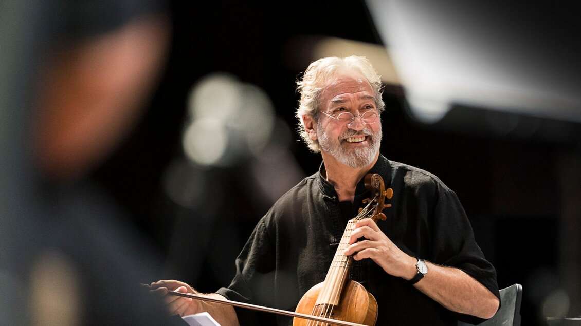 Ein lächelnder Musiker, der eine Geige hält. Er sitzt auf der Bühne und sieht glücklich aus. | © Werner Kmetitsch