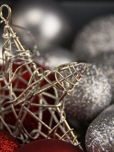 A shiny Christmas decoration with a wire star and red and silver balls. The background is festive and sparkles. | © pixabay.com