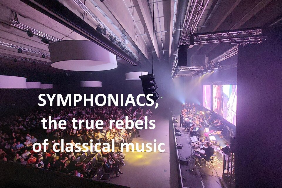 Ein Konzert mit einer großen Menschenmenge, die einem modernen symphonischen Auftritt lauscht. Auf der Bühne spielen Musiker in einem lebhaften Ambiente. | © Symphoniacs
