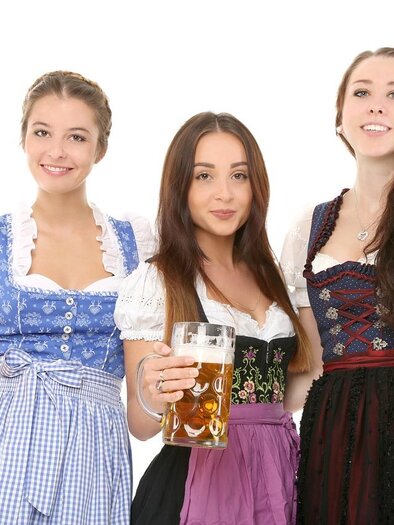 Three women in traditional Bavarian costumes are holding large beer mugs. They are smiling happily and radiate a festive atmosphere. | © Pixabay