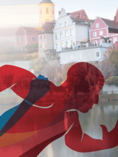 A dynamic depiction of runners in bright colors and a picturesque city view by the water. The scene conveys movement and activity in a beautiful setting. | © Stadtgemeinde Frohnleiten