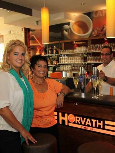 A bar with a modern decor. Two women are standing in the foreground, while a bartender is working in the background. | © Cafe Horvath
