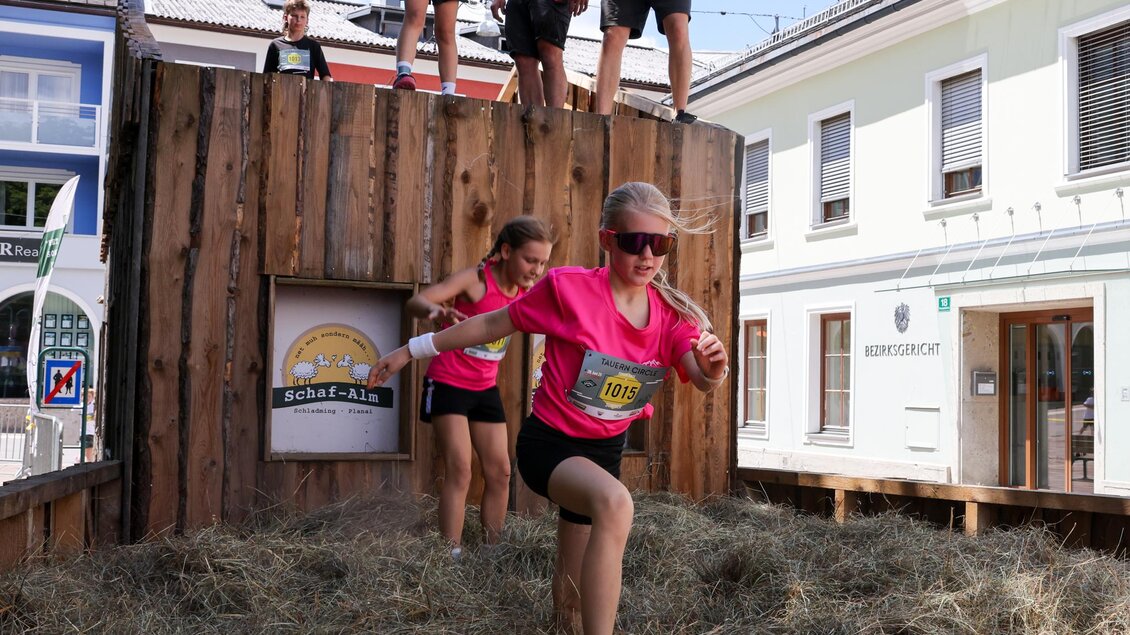 Kinder springen von einer Holzkonstruktion in eine Baustelle mit Heu. Im Hintergrund sind Erwachsene, die die Aktion beobachten. | © Hans Simonlehner