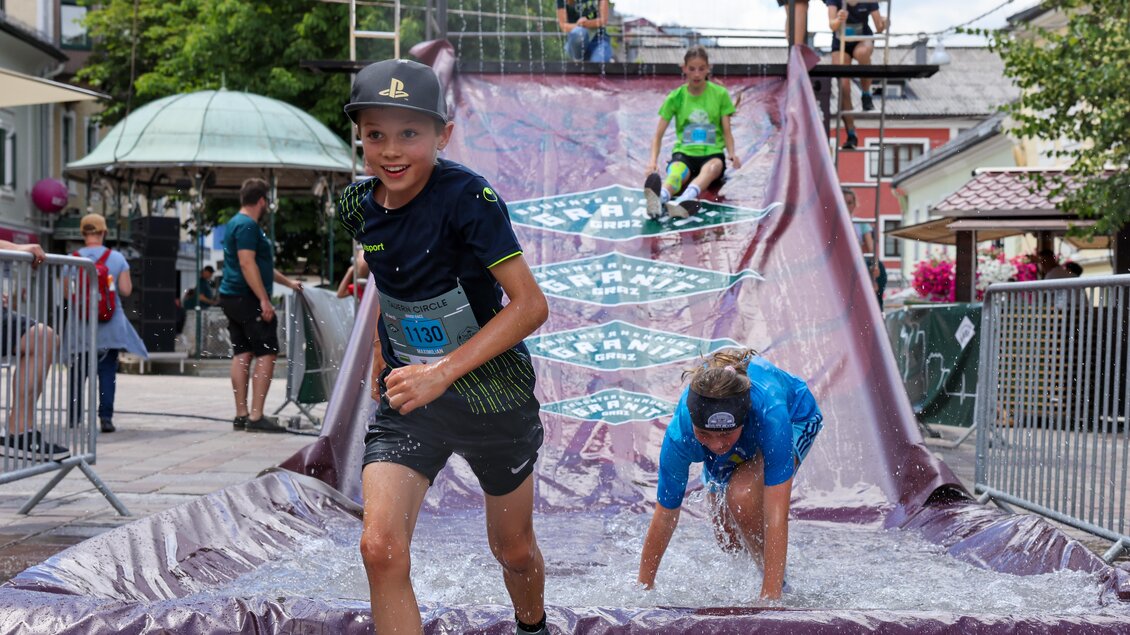 Ein spannendes Wasserrutschen-Event mit Kindern, die Freude haben. Einige Teilnehmer rutschen ins Wasser, während andere sich auf der Rutsche befinden. | © Michael Simonlehner