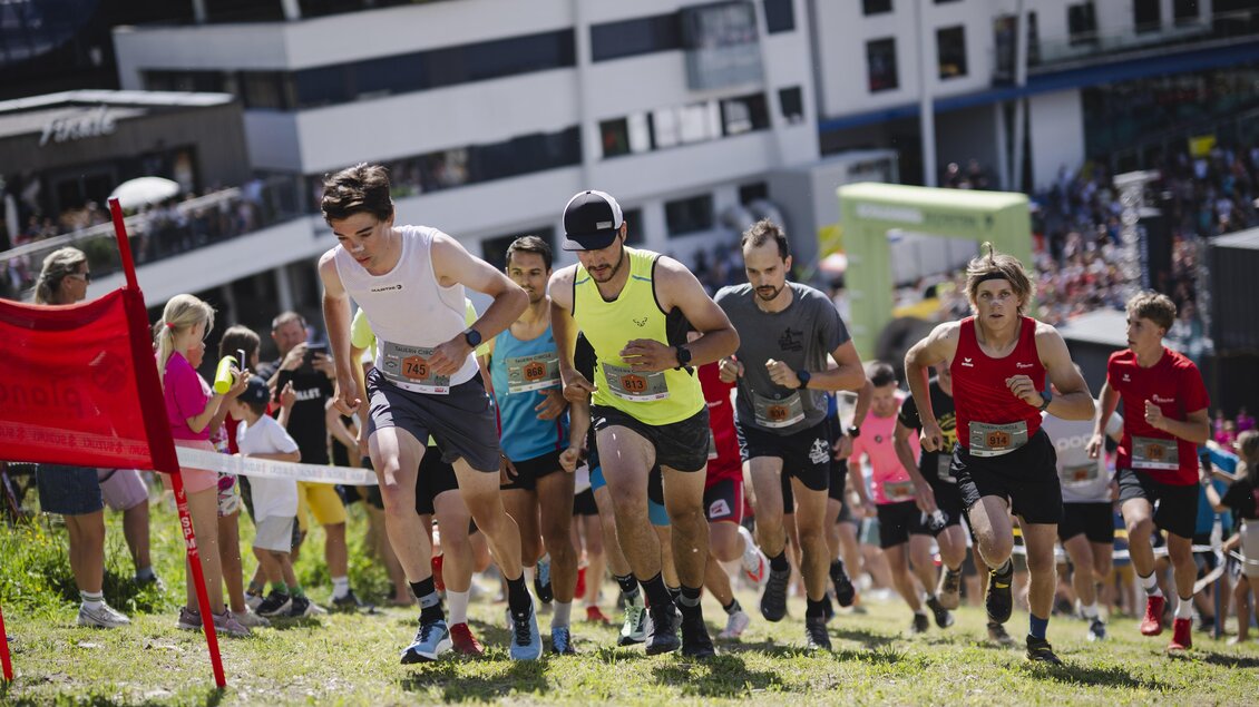 Eine Gruppe von Läufern steigt einen Hügel hinauf. Im Hintergrund sind Zuschauer und Gebäude zu sehen. | © Hans Simonlehner