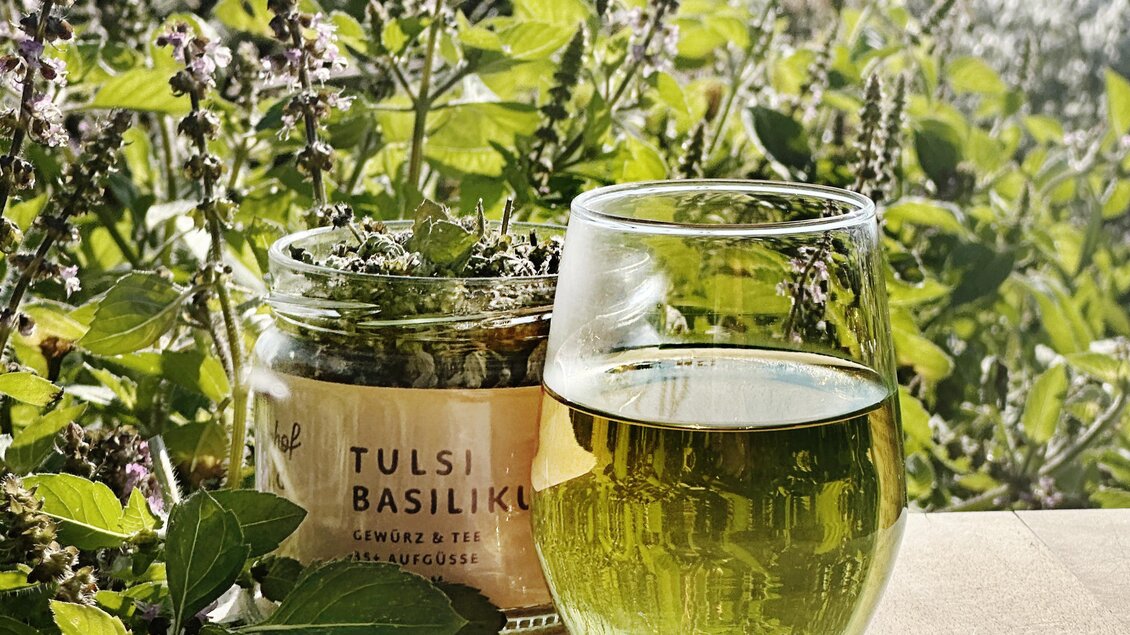 Glas mit Tulsibasilikum-Tee und Kräutermischung vom Lienhof zwischen frischen Basilikumblättern | © Lienhof