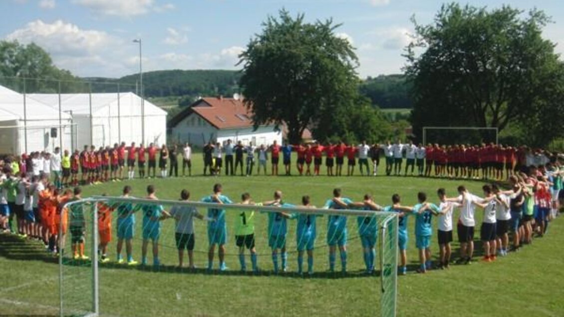 Eine Gruppe von Fußballspielern steht im Kreis auf einem Rasenplatz. Im Vordergrund ist ein Fußballtor zu sehen, während die Spieler sich gegenseitig umarmen. | © SV Leitersdorf