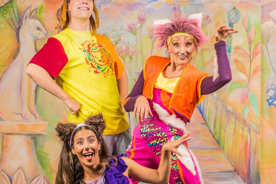 Drei fröhliche Schauspieler in bunten Kostümen posieren vor einer lebhaften Kulisse. Im Hintergrund sind Gebäude mit orientalischen Türmen und ein märchenhafter Weg zu sehen. | © Theater Heuschreck