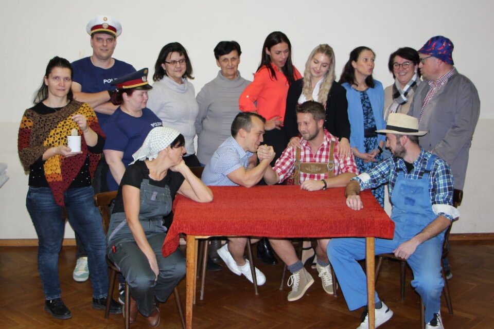 Eine Gruppe von Personen in verschiedenen Outfits versammelt sich um einen Tisch. Einige Menschen zeigen eine freundliche Interaktion, während andere zuschauen. | © Theaterverein Wir theatern wieder