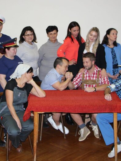 Eine Gruppe von Personen in verschiedenen Outfits versammelt sich um einen Tisch. Einige Menschen zeigen eine freundliche Interaktion, während andere zuschauen. | © Theaterverein Wir theatern wieder