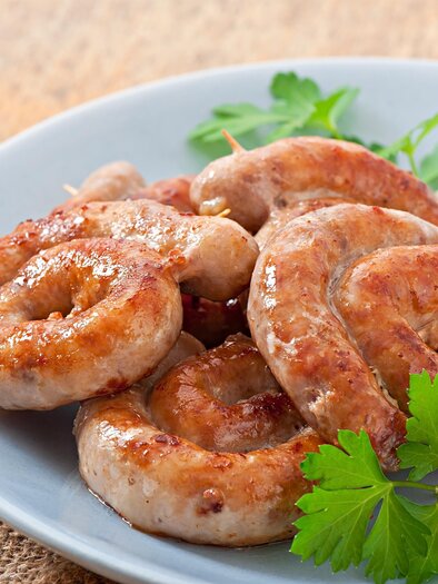 A plate with fried, spiral-shaped sausages and a small mound of rice. Fresh herbs adorn the dish. | © Maluhof Bad Waltersdorf