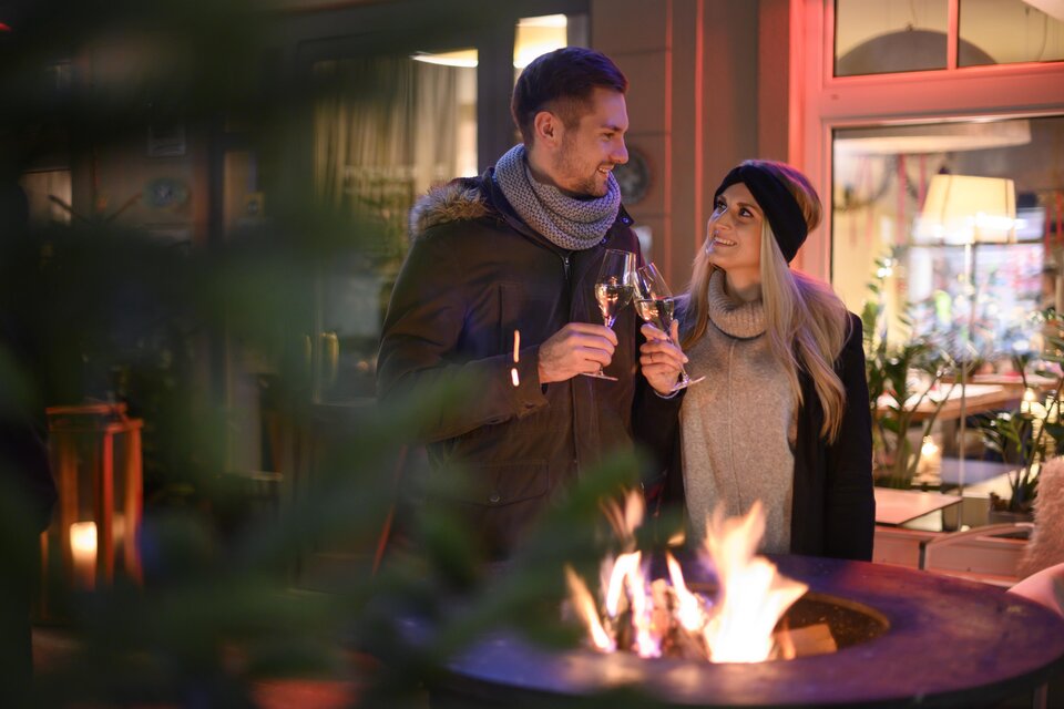 Ein Paar genießt drinks vor einem Feuerkorb in einem gemütlichen Ambiente. Die Atmosphäre ist warm und einladend. | © Bernhard Bergmann