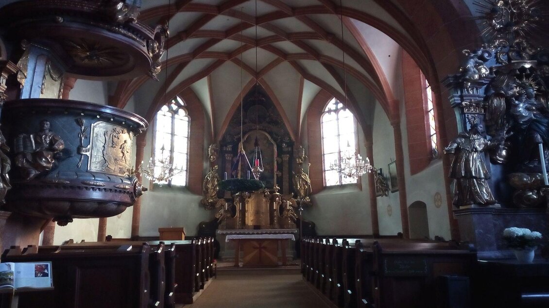 Ein lichtdurchfluteter Kirchenraum mit hohen Decken und bunten Fenstern. Die Holzbankreihen und der geschmückte Altar verleihen dem Innenraum eine ruhige Atmosphäre. | © TVB Ausserland Salzkammergut