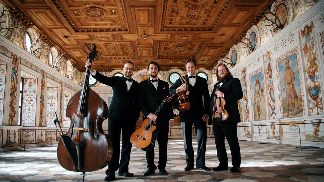 Eine Gruppe von vier Musikern steht in einem prächtigen Saal. Sie halten ihre Instrumente und sind in eleganter Abendkleidung gekleidet. | © Tyrol Music Project