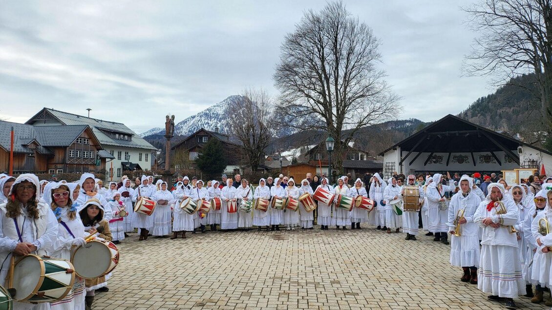 Eine Gruppe von Menschen in weißen Gewändern versammelt sich auf einem Platz. Im Hintergrund sind Berge und traditionelle Gebäude sichtbar. | ©  Martina Gaisberger