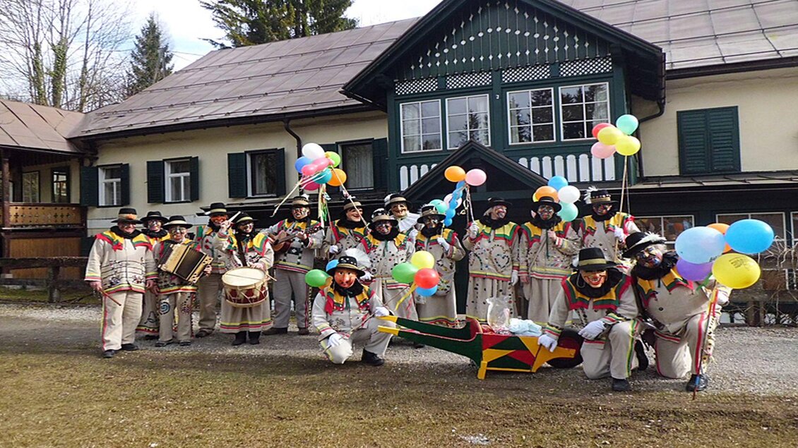 Eine Gruppe von festlich gekleideten Musikern steht vor einem Haus und hält bunte Ballons. Sie sind bereit für eine Feier oder eine Veranstaltung im Freien. | © Hermann Schröttenhamer