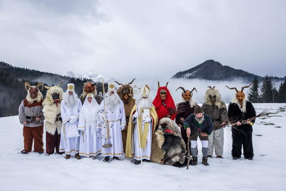 Eine Gruppe von Menschen in traditionellen Kostümen steht im Schnee. Im Hintergrund sind Berge und ein bewölkter Himmel zu sehen. | © Martin Huber