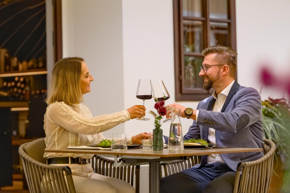 Ein Paar genießt ein romantisches Dinner in einem Restaurant. Sie stoßen mit Weingläsern an und haben eine schöne Tischdekoration. | © Der Schrenk
