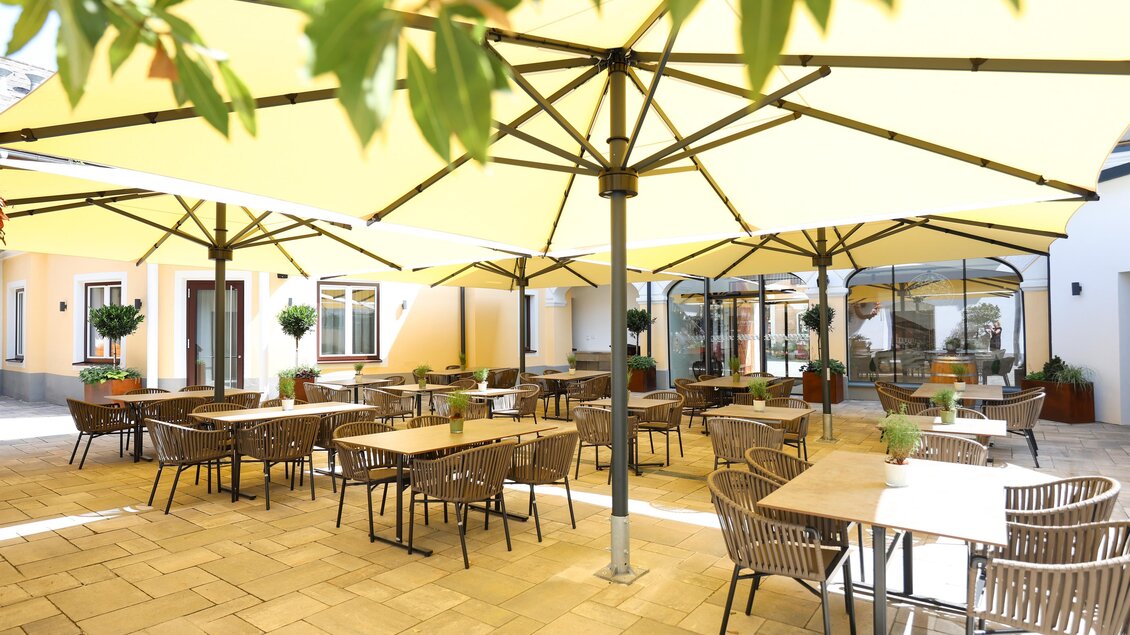 Ein gemütlicher Außenbereich mit braunen Tisch und Stühlen. Gelbe Sonnenschirme sorgen für Schatten und eine einladende Atmosphäre. | © Der Schrenk