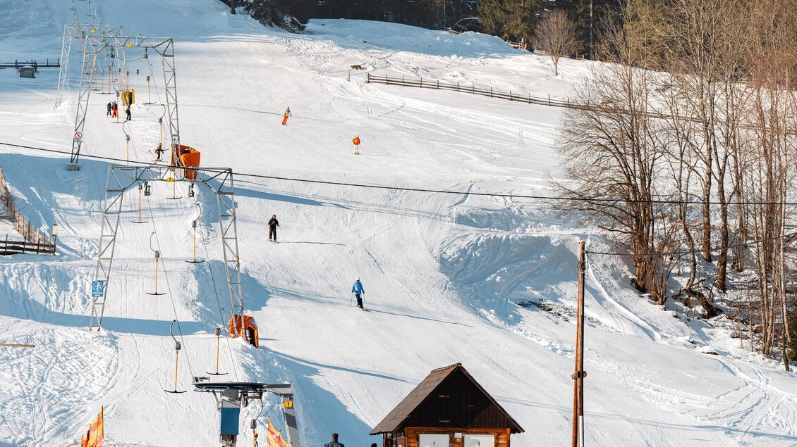 Eine schneebedeckte Skipiste mit Skifahrern und einem Skilift. Im Hintergrund sind Wälder und Berglandschaft sichtbar. | © Christoph Lukas