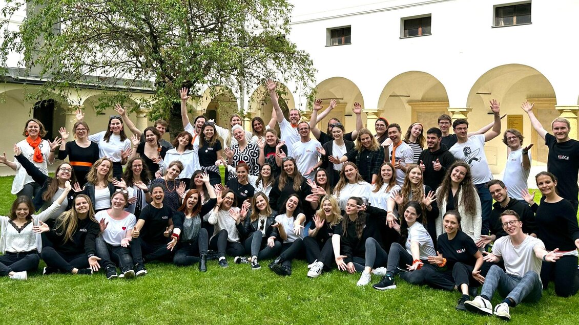 Eine große Gruppe von Menschen steht fröhlich auf einer grünen Wiese. Sie lächeln und posieren gemeinsam für ein Foto. | © Voices of Spirit – Chorverband Steiermark