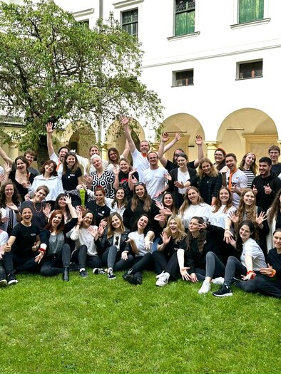 A large group of people stands happily on a green meadow. They smile and pose together for a photo. | © Voices of Spirit – Chorverband Steiermark