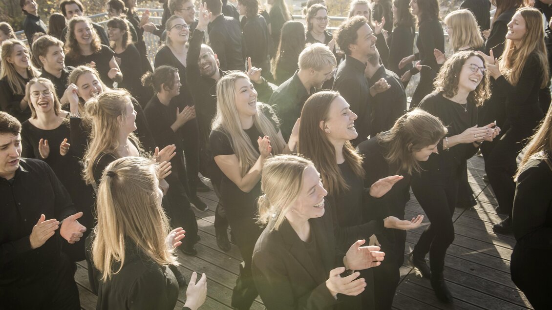 Eine Gruppe von Menschen in schwarzen Kleidern steht auf einem Terrassenbereich und applaudiert. Sie wirken fröhlich und begeistert. | © Stefan Knittel