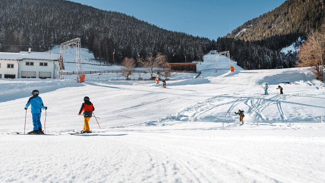 Eine verschneite Ski-Piste mit mehreren Skifahrern. Im Hintergrund sind Bäume und eine Berglandschaft zu sehen. | © Christoph Lukas