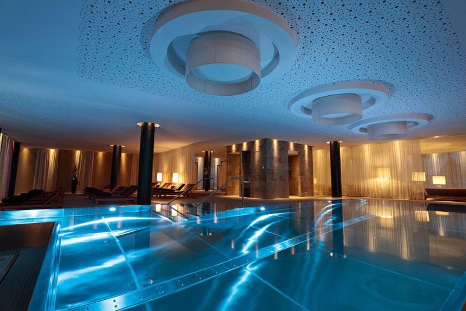 Ein elegantes Spa mit einem glitzernden Pool und modernen Deckenleuchten. Die Atmosphäre ist entspannt und einladend. | © Falkensteiner Hotel Schlasdming / Fotograf Walter Luttenberger