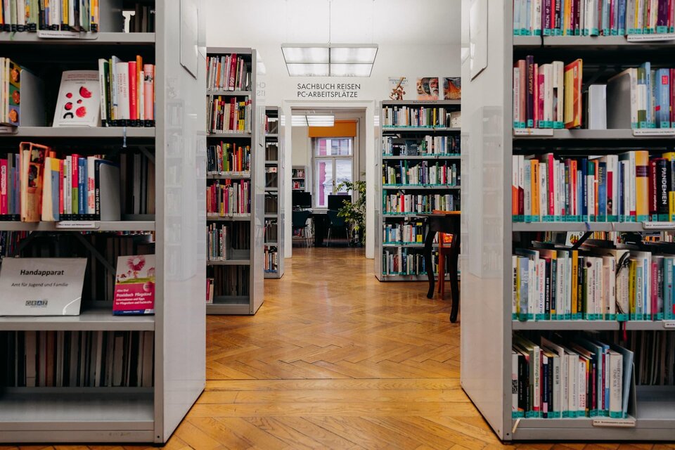 Eine gemütliche Bibliothek mit Regalen voller Bücher. Im Hintergrund sind Leseecken und Pflanzen sichtbar. | © © fotoCRafie – Christine Rechling