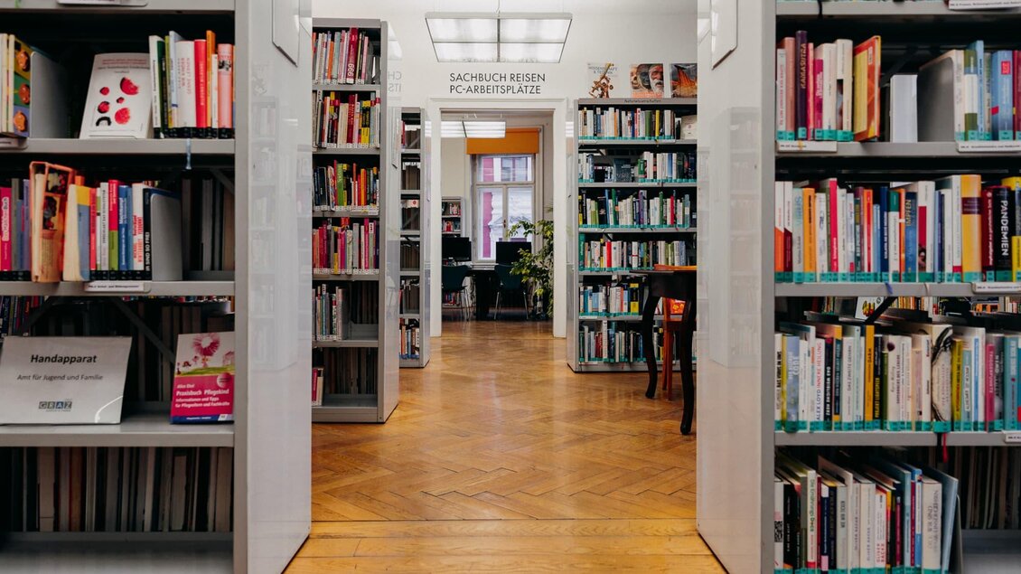 Eine gemütliche Bibliothek mit Regalen voller Bücher. Im Hintergrund sind Leseecken und Pflanzen sichtbar. | © © fotoCRafie – Christine Rechling