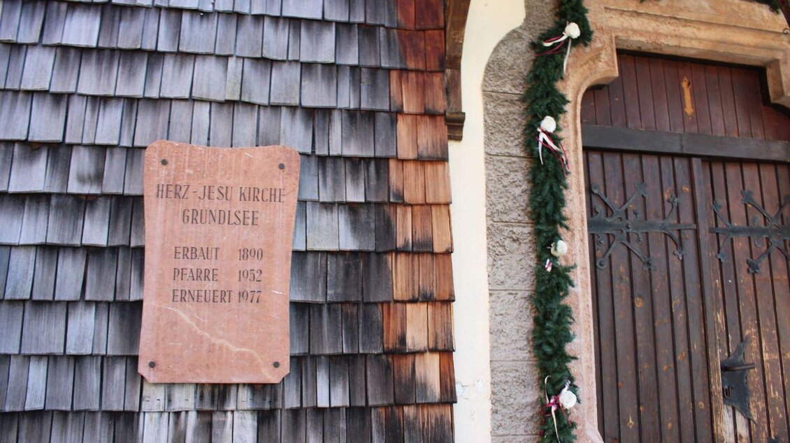 Ein rustikales Holzgebäude mit einer großen, geschlossenen Holztür. Begrüßt von Pflanzen in Kübeln und dekoriert mit einem Kranz. | © Viola Lechner