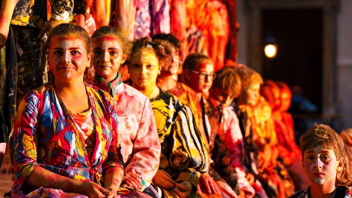 Eine Gruppe von Menschen sitzt in bunten Kleidern zusammen. Sie scheinen an einer Veranstaltung oder Aufführung teilzunehmen. | © Wandelbühne/Mediadome