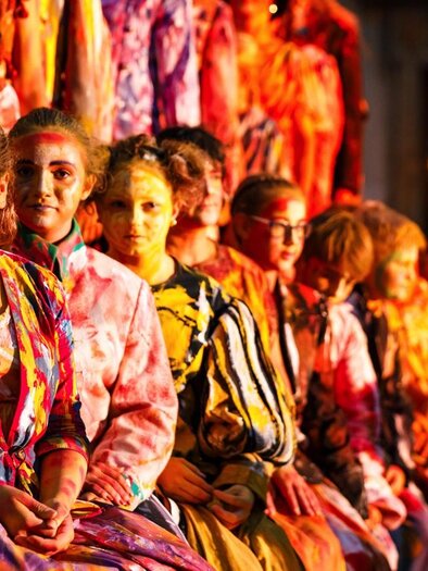 A group of people is sitting together in colorful clothing. They appear to be participating in an event or performance. | © Wandelbühne/Mediadome
