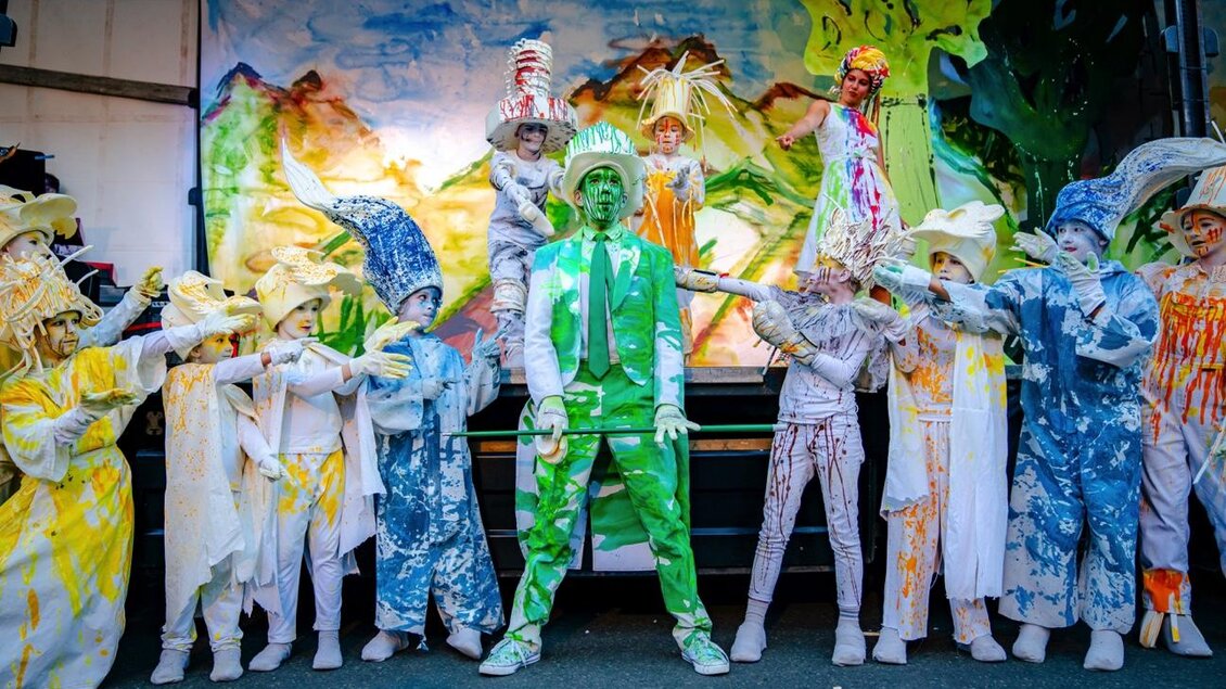 Eine bunte Gruppe von Tänzern in auffälligen Kostümen steht auf einer Bühne. Die zentralen Figuren sind grün und spielen mit Farben und Formen. | © Wandelbühne/Philine Hofmann