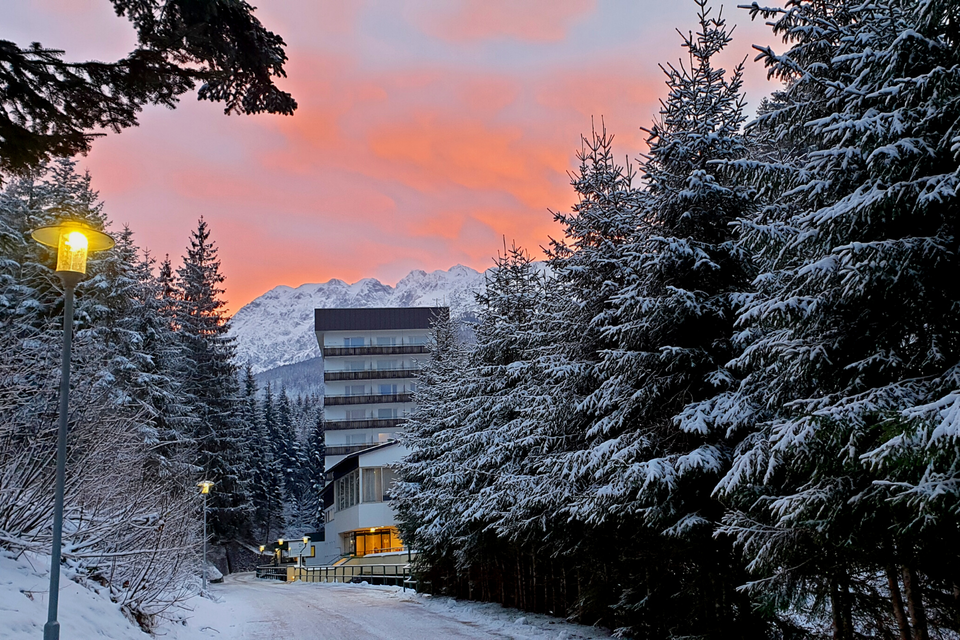 Ein Bergresort umgeben von schneebedeckten Bäumen. Der Himmel erstrahlt in sanften Rosa- und Lilatönen bei Sonnenuntergang. | © Daniela Casari