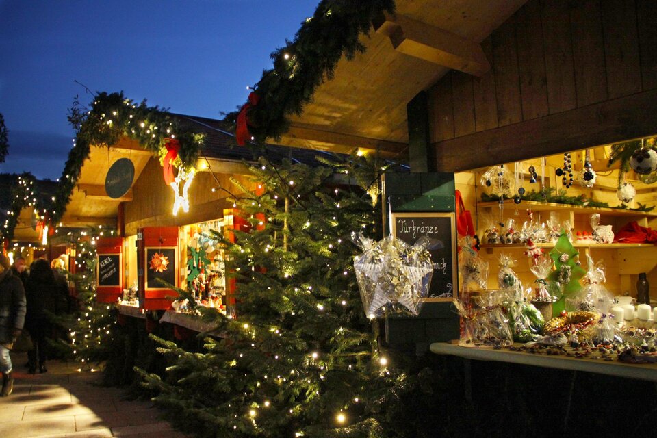 Ein festlicher Weihnachtsmarkt mit beleuchteten Ständen und einem geschmückten Weihnachtsbaum. Die Umgebung ist stimmungsvoll und einladend. | © A. Pech
