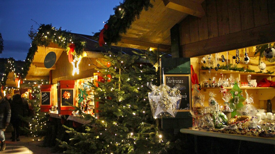 Ein festlicher Weihnachtsmarkt mit beleuchteten Ständen und einem geschmückten Weihnachtsbaum. Die Umgebung ist stimmungsvoll und einladend. | © A. Pech