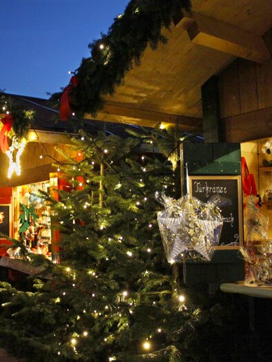 A festive Christmas market with illuminated stalls and a decorated Christmas tree. The atmosphere is charming and inviting. | © A. Pech