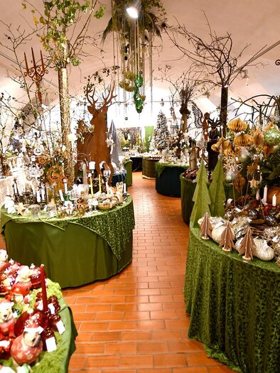 A beautiful shop adorned with various decorations and plants. The tables are covered with green cloths and offer a variety of festive items. | © Tourismusverband Thermen- & Vulkanland/Christian Thomaser