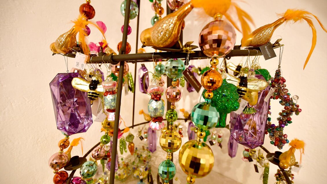Eine dekorative Kette mit bunten, glitzernden Ornamenten und Vögeln. Sie hängt an einem Ständer und strahlt festliche Farben aus. | © Tourismusverband Thermen- & Vulkanland/Christian Thomaser