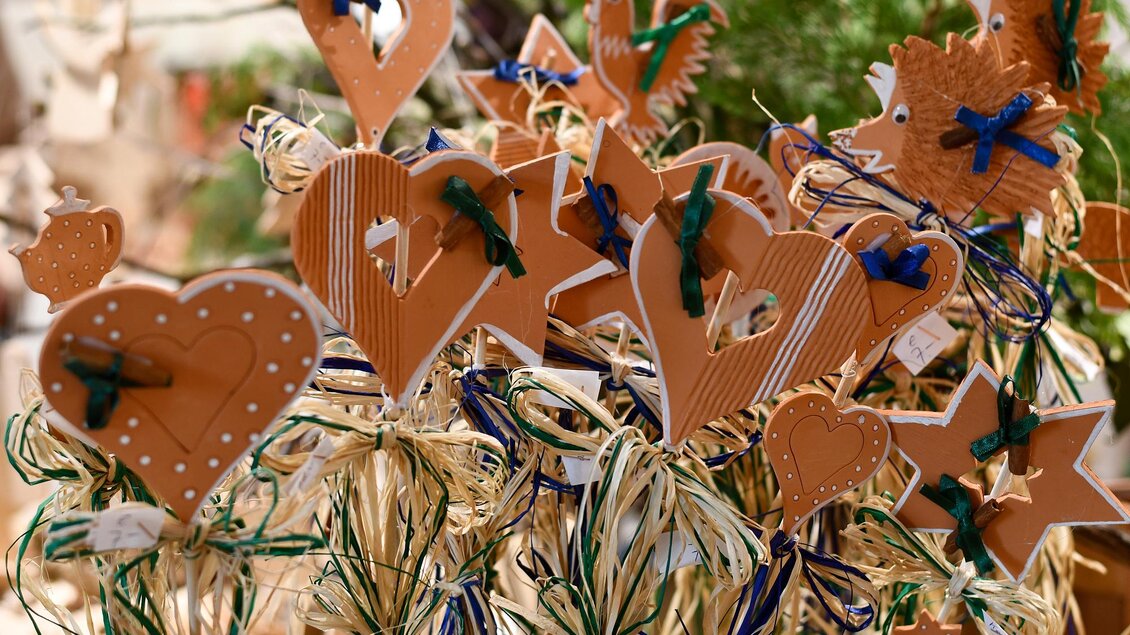 Bunte Holzornamente in Form von Herzen und Sternen mit Schleifen aus Stroh. Die Dekoration wirkt festlich und einladend. | © Tourismusverband Thermen- & Vulkanland/Christian Thomaser