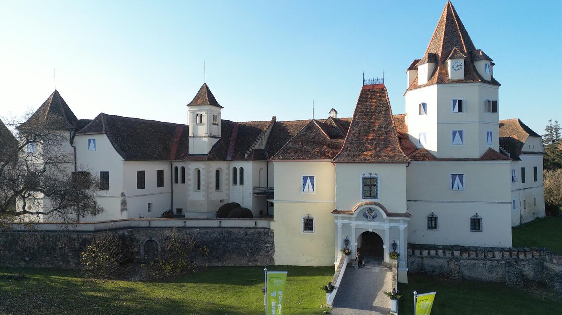 Ein beeindruckendes Schloss mit Türmen und einer malerischen Fassade. Der grüne Garten und der klare Himmel verleihen der Szene eine schöne Atmosphäre. | © Tourismusverband Thermen- & Vulkanland/Christian Thomaser