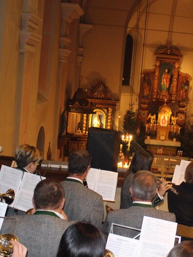 Ein Blasorchester spielt in einer Kirche. Im Hintergrund sind religiöse Bilder und eine Altarkreuz zu sehen. | © Musikverein Unterlamm