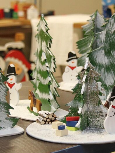 A festive Christmas landscape with handcrafted snowmen and pine trees. In the foreground, gifts and wooden figures can be seen. | © Pixabay